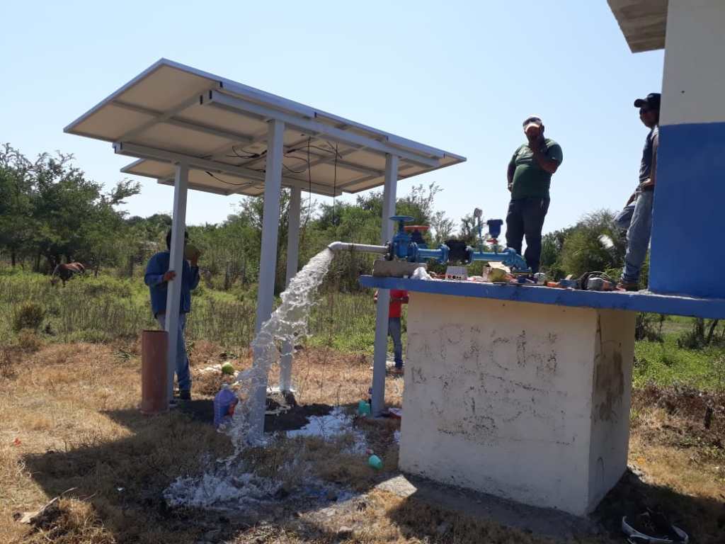 **Summary** The image depicts a solar panel system operating a pump in a field on a bright, sunny day. **Alt Text**: Un tr...