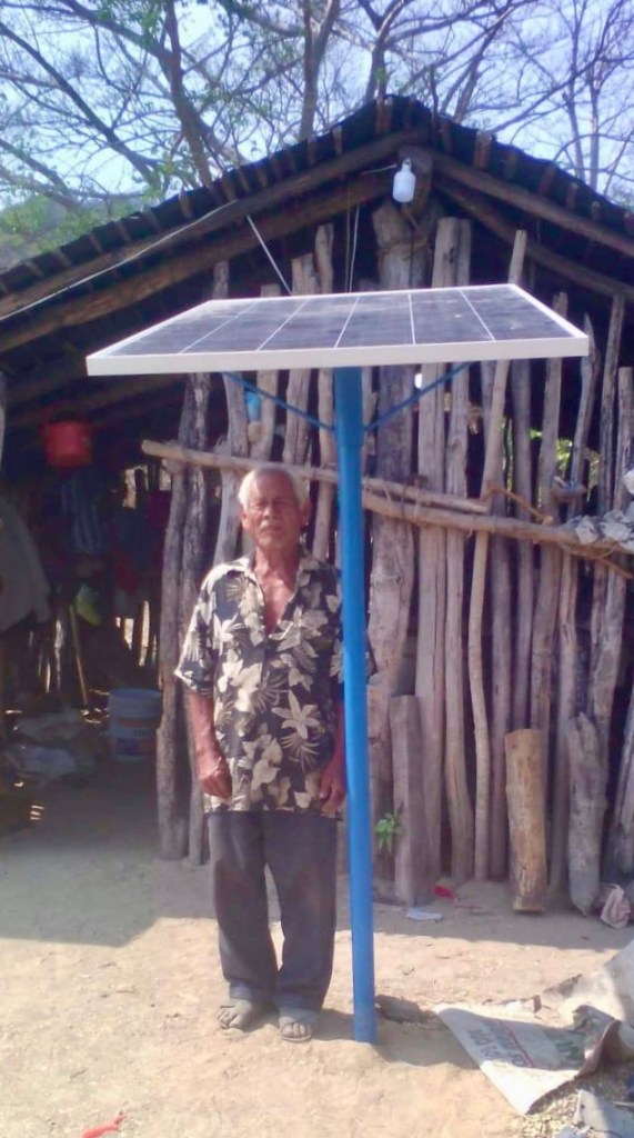 Un hombre parado debajo de un sol ardiente al lado de un panel solar en la calle, con un cielo claro en el fondo venido de...